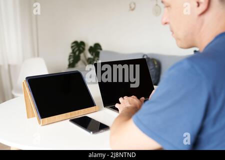 A serious person who works remotely at home. A man enters information into a laptop. Layout concept, design. Black screens on laptops and tablets. Layout for your design. High quality photo Stock Photo