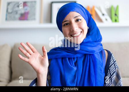 Portrait of smiling young Muslim woman talking to camera from home. Videoconference with friend or family member, online interview or work meeting, vl Stock Photo