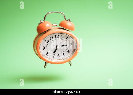 Orange vintage style flying alarm clock. Flying alarm clock on green background. Stock Photo