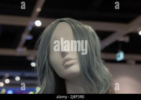 The head of white female mannequin with gray hair against a dark ceiling with white beams. Close-up photo. Soft focus. Stock Photo