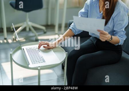 self employed, business owner, pleasure from work, Asian woman using computer holding financial documents to check or plan budget, manage investment Stock Photo