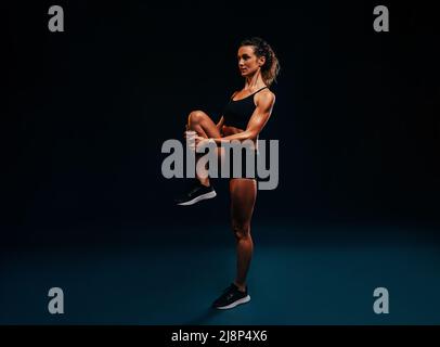 Sports woman doing flexibility exercises. Young female runner stretching her leg. Stock Photo