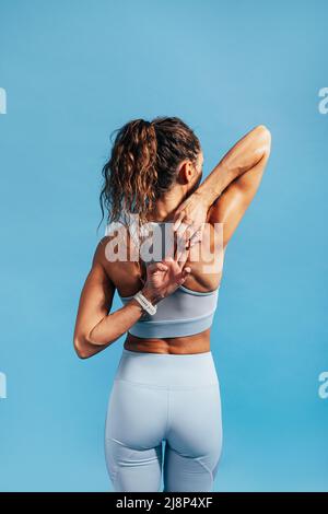 Back view of fitness woman stretching her hands against blue background, warming up Stock Photo