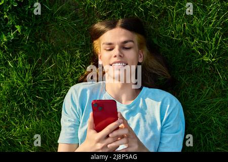Young guy with smartphone in his hands on green grassy background Stock Photo