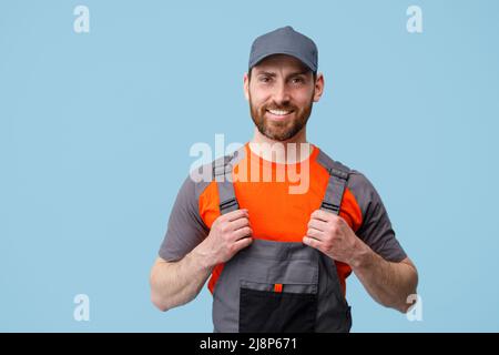 Portrait of smiling builder in uniform holding on his jumpsuit and looking at camera Stock Photo