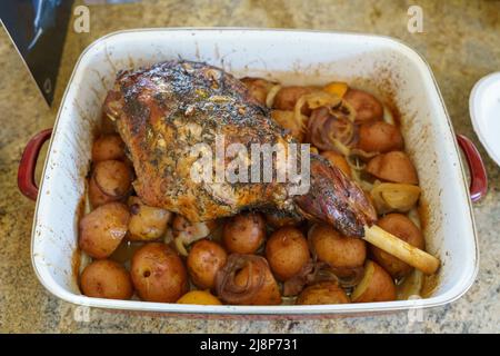 Leg of lamb on top of roasted potatoes in a white pan Stock Photo