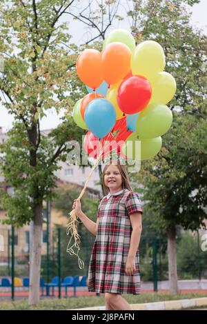 charming teenage girl in checkered brown dress with bunch of colorful balloons. school girl. pretty tween. Stock Photo