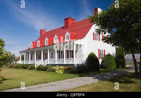 Old circa 1825 Canadiana cottage style home with white wood plank cladding and red painted cedar wood shingles roof. Stock Photo