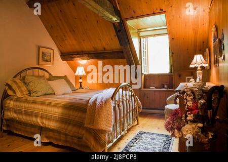 Brass bed and antique furnishings in guest room on upstairs floor inside old circa 1740 Canadiana cottage style home. Stock Photo