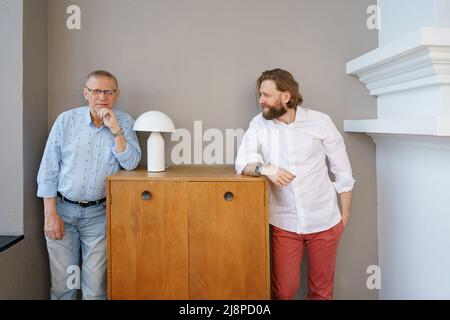 Father and son stand on opposite sides of the pedestal in the living room, the son looks at the father, an elderly man in glasses with diopters, a