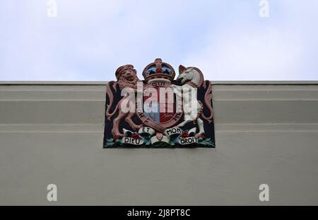 Royal coat of arms of the United Kingdom, at the top of the white exterior wall of a building, with cloudy sky in the background Stock Photo