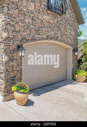 Vertical White puffy clouds Double arched sectional garage doors with potted plants outside Stock Photo