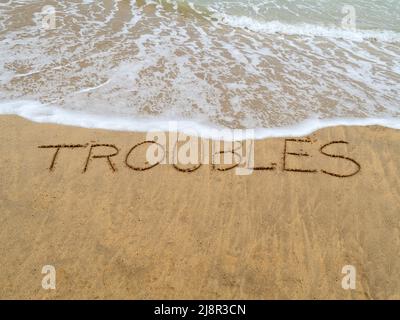 Concept image - to illustrate washing away stress by taking a vacation as waves on a sandy beach wash away the word 'troubles' written in sand. Stock Photo