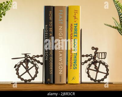 Novelty bicycle bookends made from a bicycle chain supporting 3 cookbooks on Kitchen shelf Stock Photo