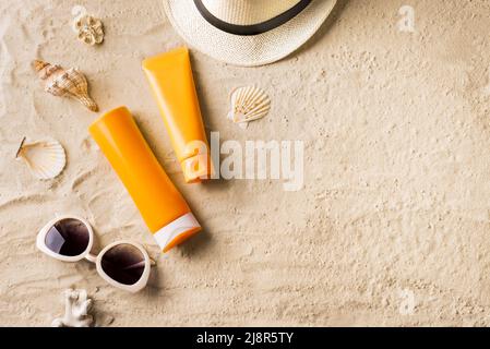 Summer travel beach flat lay composition, copy space. Sunglasses, sunscreen lotion, sunblock cream and seashells on beach sand background. Summer vaca Stock Photo