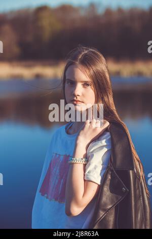 Portrait of a beautiful happy teenage girl outdoors in spring. A girl poses on lakes shore. Stock Photo