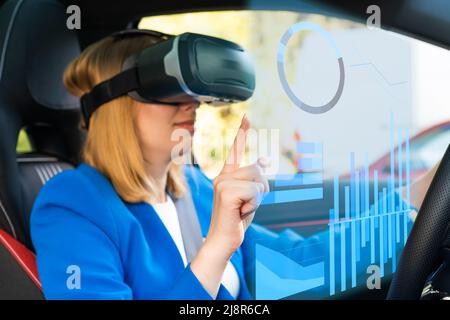 Digitally generated graphics and charts interface managed by business woman in vr googles sitting in the car in a blue suit. Metaverse cyber world technology concept.  Stock Photo