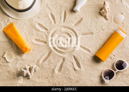 Summer travel beach flat lay composition. Wicker hat, sunglasses, sunscreen lotion, sunblock cream and seashells on beach sand background. Summer vaca Stock Photo