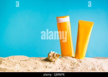 Sunscreen lotion on sandy beach, blue background, copy space. Summer vacation and skin care concept, spf uv-protect cosmetics. Stock Photo