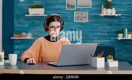 University student using headphones and laptop to attend online class on video call meeting. Woman talking to teacher on remote videoconference for educational live communication. Stock Photo