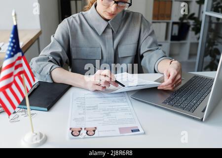 High angle shot of mature Caucasian woman wearing grau shirt sitting at desk in office working with visa application papers Stock Photo