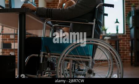 African american man in wheelchair using headset on phone line, discussing about telemarketing and sales with clients on helpline service. Male employee working at call center office. Stock Photo