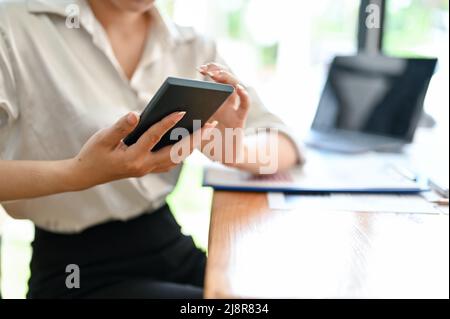 Female sitting at her office desk, using smartphone, chatting with colleagues, contact a business supplier. cropped image Stock Photo