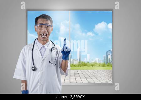 Asian nerd scientist with a stethoscope standing and pointing at something with a window glass background Stock Photo