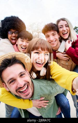 Vertical photo of Cheerful group of happy friends taking smiling selfie in piggyback. Three couple having fun together outdoors at park in the city Stock Photo