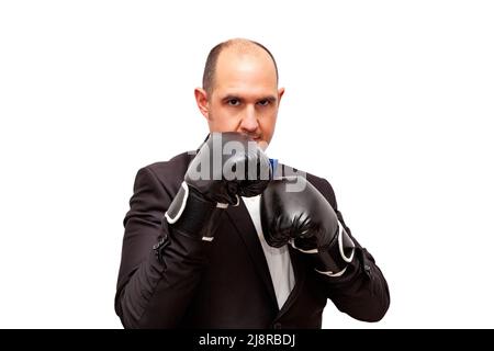 A bald adult Caucasian male dressed in a suit, shirt and bow tie is wearing black boxing gloves and is in a fighting stance. The background is white. Stock Photo
