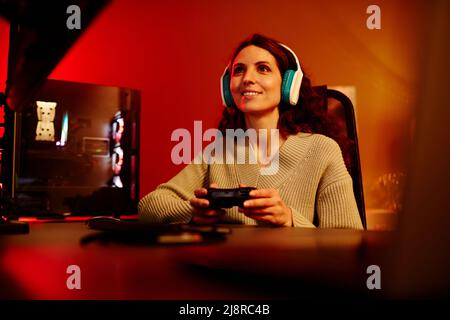 Modern young adult Caucasian woman playing racing or shooter video game using console in living room at night Stock Photo