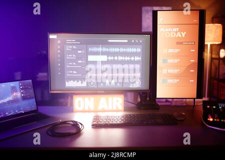Horizontal no people shot of modern amateur radio broadcast or podcast station interior, desktop computer, laptop and mixer on table at night Stock Photo