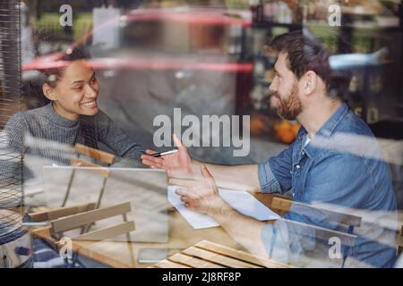 Happy smiled couple of startupers talking and sharing ideas at table in cafe. Business meeting. Stock Photo