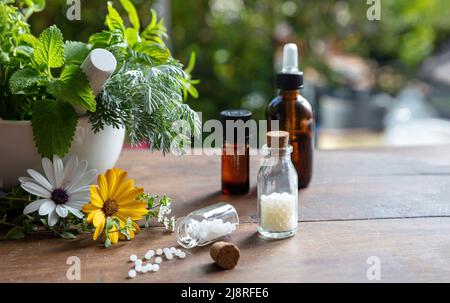 Homeopathy pharmacy, herbal, natural medicine. Homeopathic globules scattered out of a glass bottle, fresh herb in a mortar, green nature background. Stock Photo