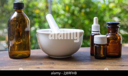 Natural pharmacy and homeopathy products. White mortar and pestle and glass medicine bottles on wooden table, blur nature background Stock Photo