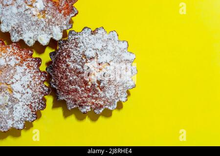 Freshly baked cupcakes sprinkled with powdered sugar on a yellow background. View from above. Culinary theme. Stock Photo