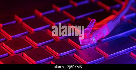 RJ45 internet cable on computer keyboard with neon lights. copy space Stock Photo