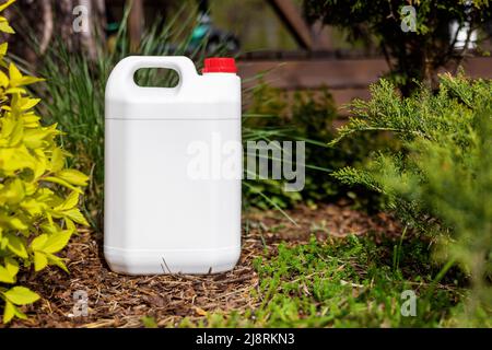 white blank plastic jerry can for garden plant fertilizer in flower bed Stock Photo