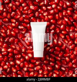 White plastic tube with pomegranate cream on red ripe garnet seeds. Natural organic cosmetic product packaging design, branding. Stock Photo