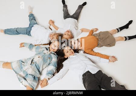 Aerial view of happy smiling school kids lying in circle and looking at camera. Beauty, kids fashion, education, happy childhood concept. Stock Photo