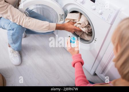 cropped view of man holding measuring cup with blue detergent near washing  machine with dirty Stock Photo by LightFieldStudios