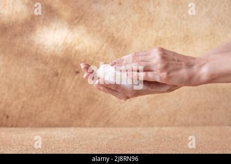 Woman hands touching foamy soap on beige background for spa advertising Stock Photo