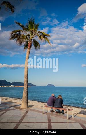 Mature couple sitting in Albir (L´Albir) beach promenade at sunset, Alicante, Spain Stock Photo