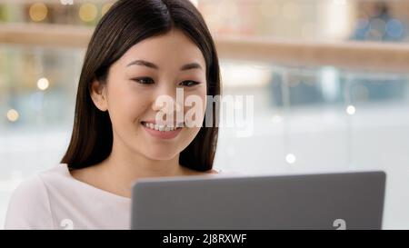 Portrait smiling happy asian female face looking at laptop satisfied girl woman freelancer boss worker manager typing computer using shopping app serv Stock Photo
