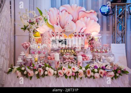 Delicious desserts at the wedding candy bar in the buffet area: decorated candles, rosebuds, ribbons, macaroons, strawberries in white chocolate. Stock Photo