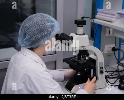 Kazan, Russia. May 10, 2022. Researcher looking through microscope in laboratory. Laboratory glassware containing chemical liquid for researching biol Stock Photo