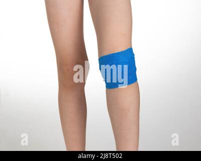 Blue elastic bandage on the knee joint on the child's leg. White background, treatment of knee pain and sprain Stock Photo