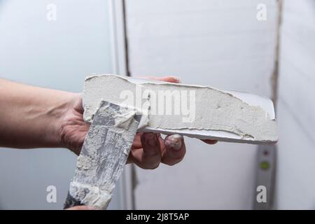 Applying glue to a white decorative gypsum brick. Brick laying on the wall Stock Photo