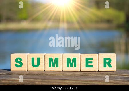 Word SUMMER made from wooden alphabet blocks against a lake background. Summertime vacation concept. Stock Photo