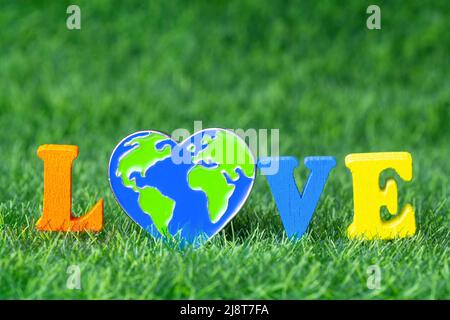 Word LOVE made from color letters and a heart shaped globe pin on a green grass background. Creative Save Planet concept. Stock Photo